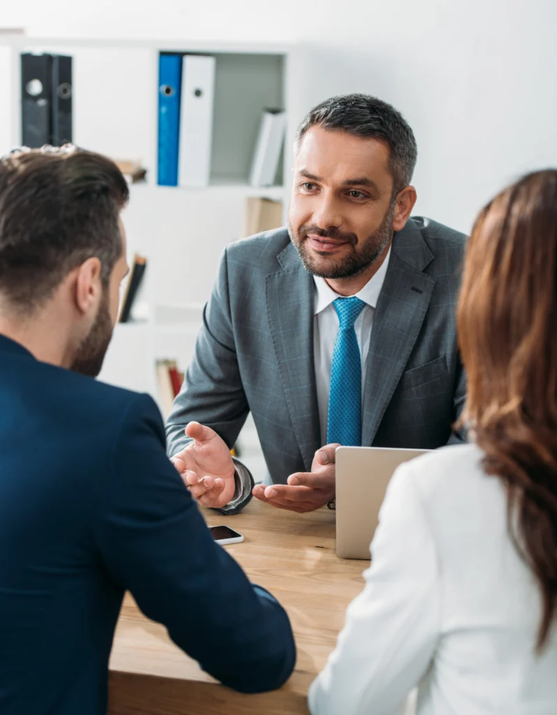 selective focus of handsome advisor in suit talking with investors at workspace